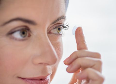 close up of an attractive mature lady putting on contact lenses in her green eyes