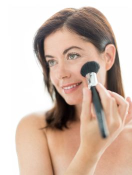 portrait of a beautiful mature lady in her forties using professional brush to apply powder on cheekbones