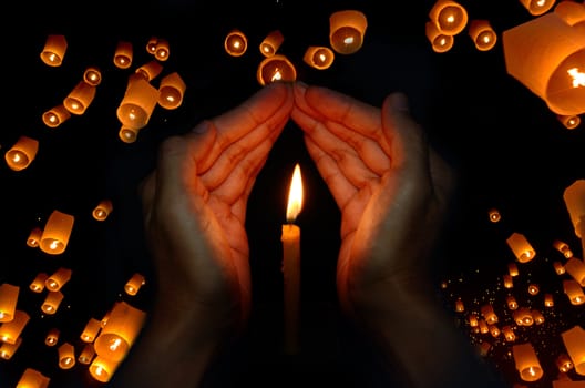 Candle light in hand with Floating lantern in the night sky background, Pray concept