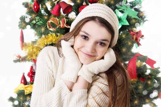 Pretty teenage girl in knitted mitten and hat under Christmas tree