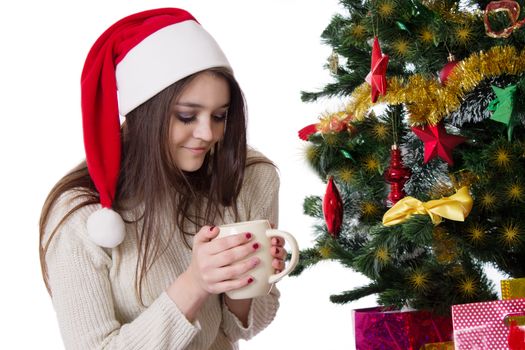 Pretty teenage girl with coffee mug under Christmas tree over white