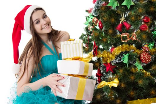 Smiling Santa helper girl with pile of presents under Christmas tree
