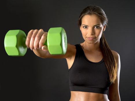 Photo of a beautiful female doing a front shoulder fly with a dumbbell over a dark background.