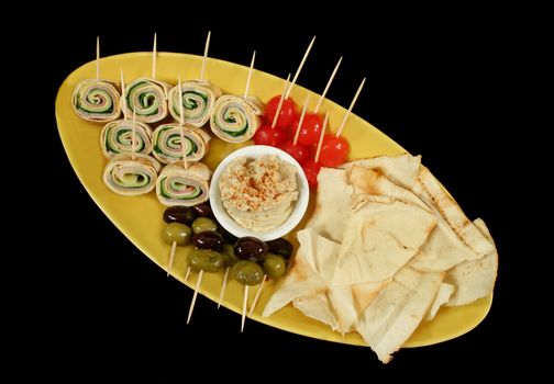 Plate of party food consisiting of olives, pickle onions, pita bread, hummus and ham and cheese roll ups.