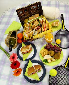 Selection of food for a picnic with a hamper, basket, fruit, wine and tennis racquets.