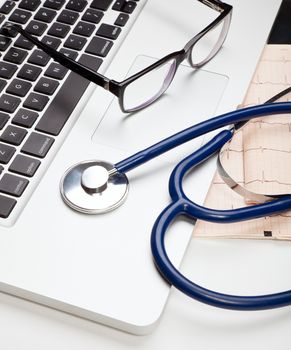Stethoscope and glasses lying on laptop computer
