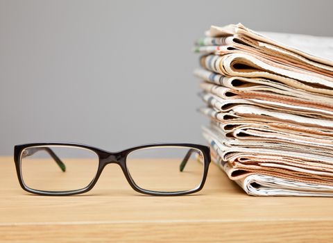 News concept Glasses on a table with stack of newspapers