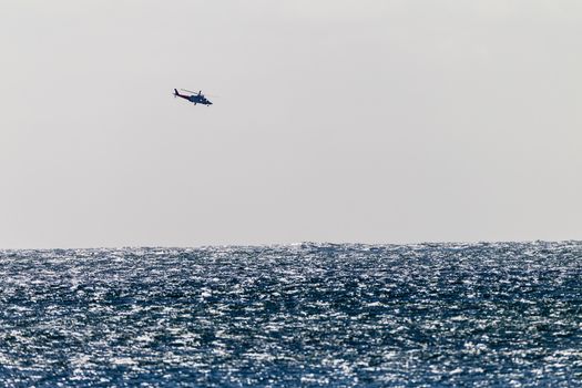Distant helicopter flying over ocean in high storm winds making water chops on sea water.
