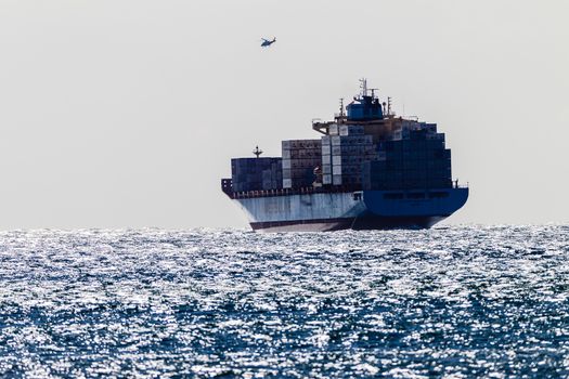 Container ship with pilot helicopter assist in high storm winds over the sea ocean.