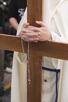 Penitent supports their hands crossed with a rosary on a wooden cross in holy week, Spain