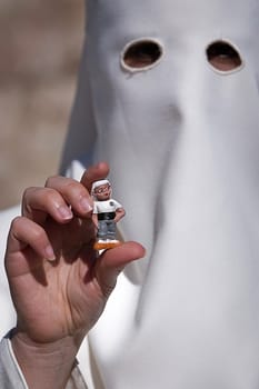 Penitent with a costalero figurine in his hand during Holy Week, Spain