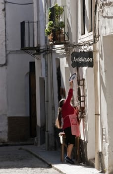 Woman hanging a ceramic plate on the door of a shop of antiques, Ubeda, province Jaen, Andalusia, Spain