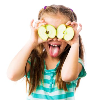 little girl with two halves of an apple near her eyes shows tongue isolated on white background
