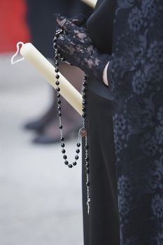 Detail of a woman dressed in mantilla holding a rosary and a candle during a Holy week procession, Spain