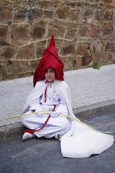 Penitent resting sitting on the ground during an Easter procession, Andalucia, Spain
