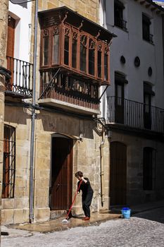 House and traditional balcony in Ubeda, woman cleaning the entrance on a sunny day, Ubeda, Jaen province, Andalusia, Spain