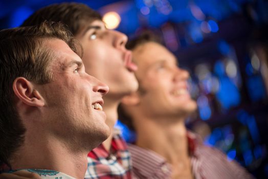 Three men stand in a row embracing smile and look in front of you, sports fans