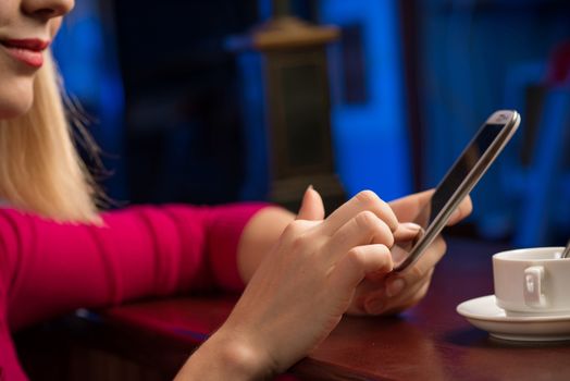 close-up of female hands holding a cell phone, sitting at the bar, next to a cup of coffee