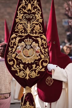 Detail penitent holding a banner with the coat of arms of the brotherhood during Holy Week, andalusia, Spain