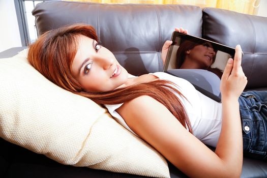 A young woman using a Tablet PC while laying on the sofa.