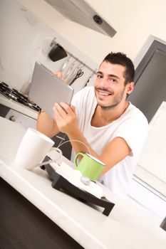 A young male sitting in the kitchen with a Tablet PC.