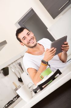 A young male sitting in the kitchen with a Tablet PC.