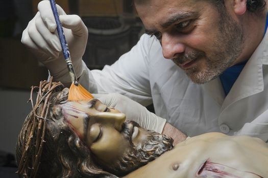 Cleaning of the face of a wooden sculpture of Christ crucified with a fan brush, Andalusia, Spain