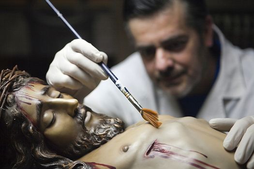 Cleaning of the face of a wooden sculpture of Christ crucified with a fan brush, Andalusia, Spain