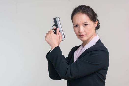 Portrait of woman in business suit holding a hand gun with agent pose on grey background