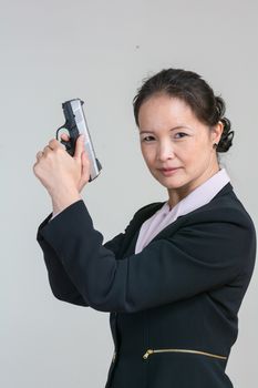 Portrait of woman in business suit holding a hand gun with agent pose on grey background