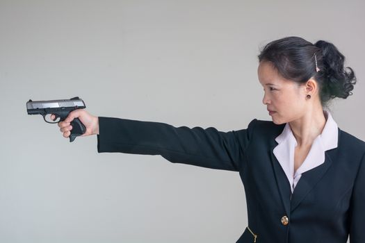 Portrait of woman in business suit aiming a hand gun on grey background