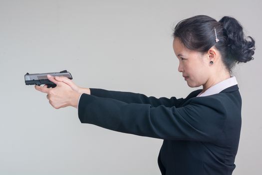 Portrait of woman in business suit aiming a hand gun on grey background