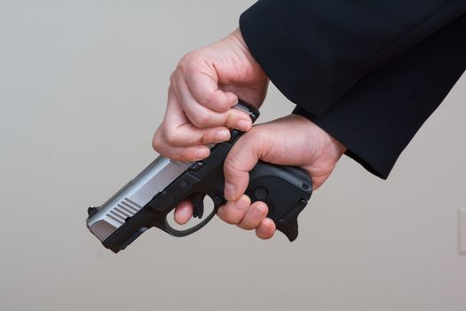 Close up of woman in business suit cocking a hand gun on grey background