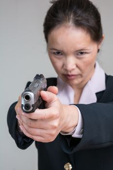 Close up portrait of woman in business suit aiming a hand gun