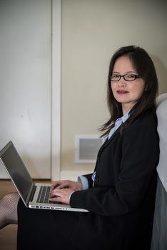 Woman in business suit with laptop sitting on the floor of a bedroom
