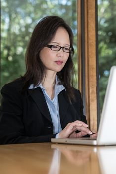 Woman in business suit with laptop on desk typing and searching in front of a window