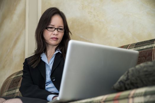 Woman in business suit typing on laptop while sitting on a sofa