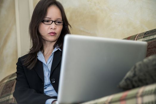 Woman in business suit typing on laptop while sitting on a sofa