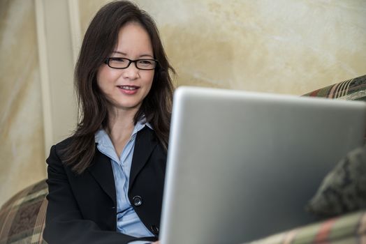 Woman in business suit typing on laptop while sitting on a sofa