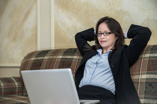 Woman in business suit laying back on a sofa while watching a laptop