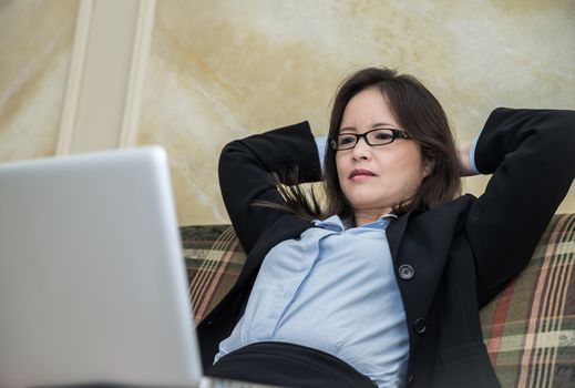 Woman in business suit feeling tired and yawning on sofa with labtop