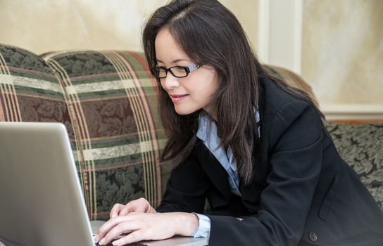 Woman in business suit relaxing on sofa and typing on laptop at home 