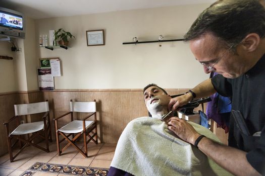 Barber shaving with a razor to young man in a barber's shop, Sabiote, Jaen province, Andalucia, Spain