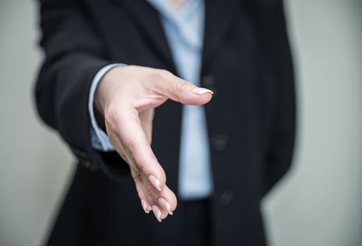 Professional woman in business suit ready for hand shake with grey background 