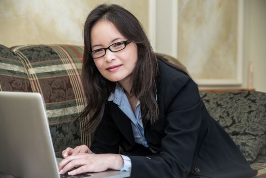 Woman in business suit relaxing on sofa and typing on laptop at home 