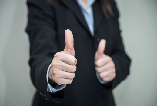 Professional woman in business suit giving thumbs up in approval on grey background 