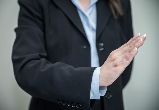Professional woman in business suit signals denial with one hand on grey background 