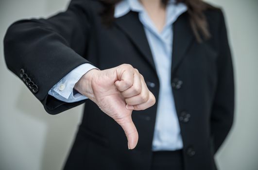 Professional woman in business suit giving thumbs down in disapproval on grey background 