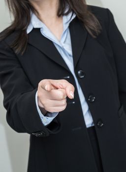 Professional woman in business suit pointing at you with one finger on grey background 