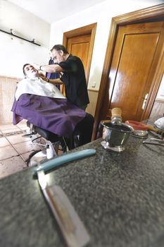 Barber shaving with a razor to young man in a barber's shop, Sabiote, Jaen province, Andalucia, Spain